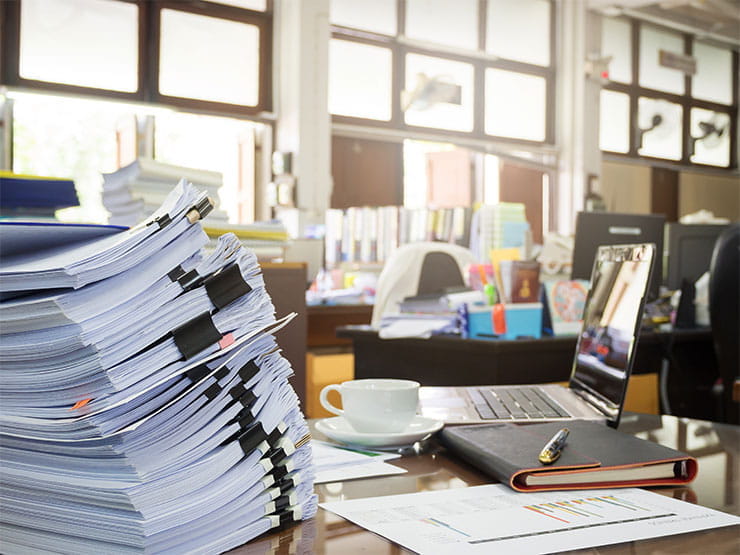 Cluttered desk with large stack of papers in foreground