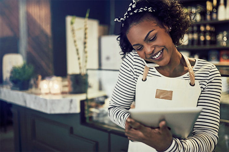 Woman in apron at café on phone using tablet