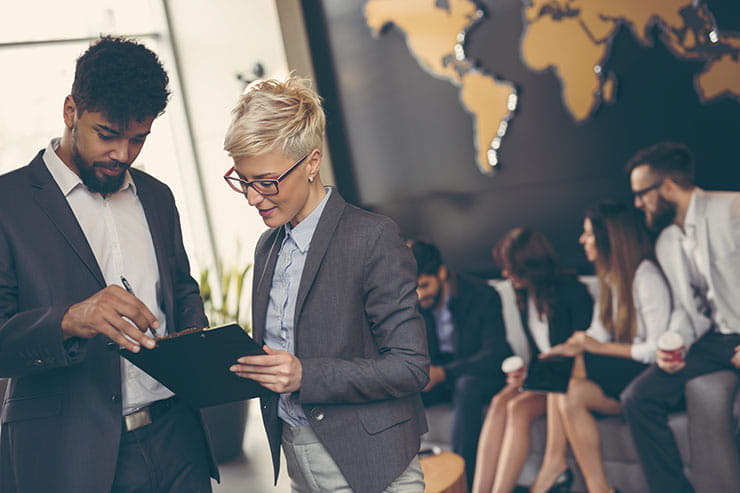 Two employees reading a clipboard standing in front of a map